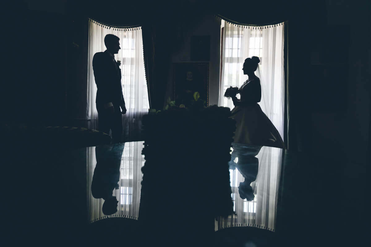 Esküvő fotózás során készült kép egy Juditról és Tamásról. Félhomályban állnak egymás mellett.